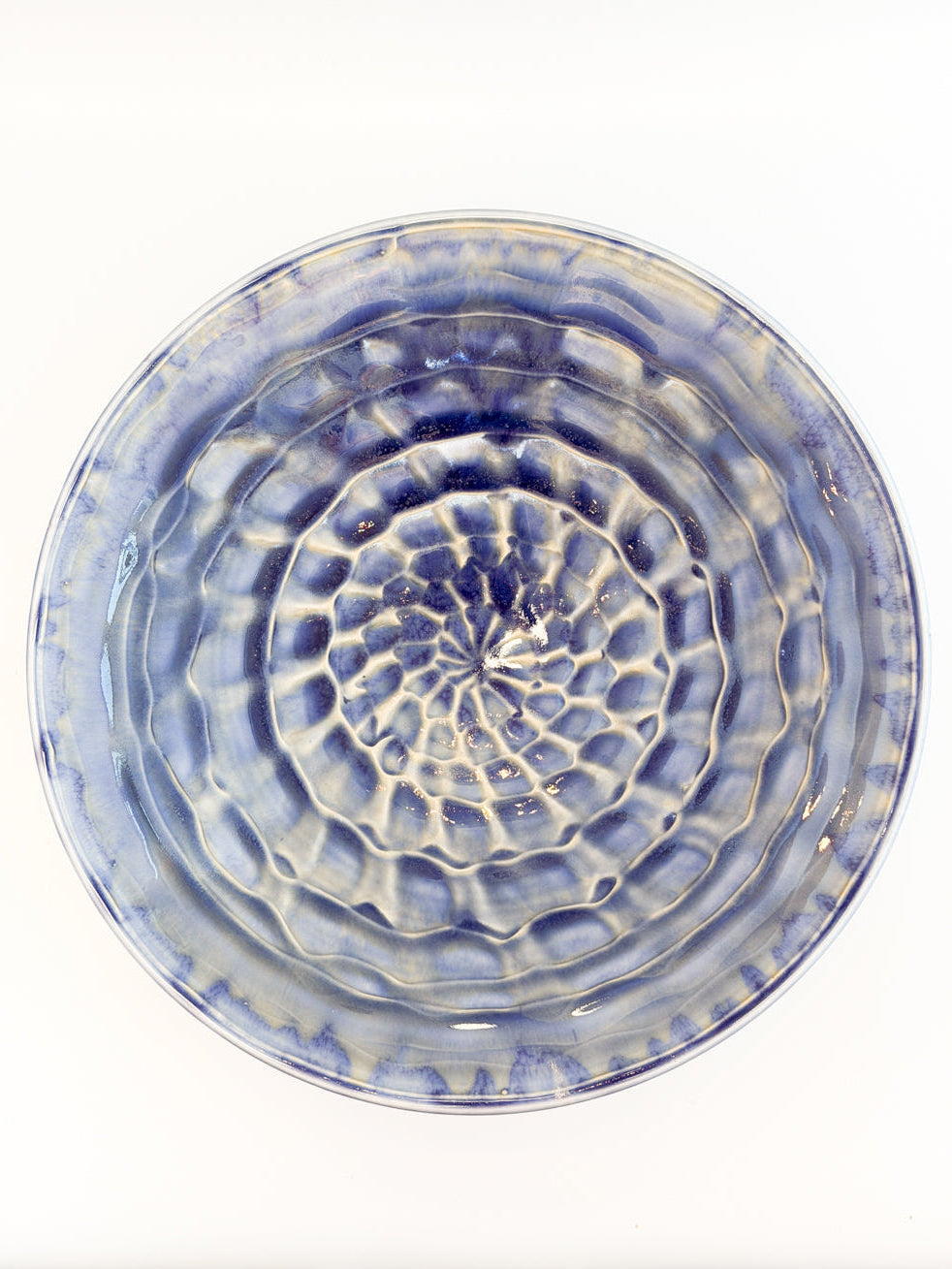 A round ceramic plate with a textured, concentric ripple pattern in blue and white glaze, photographed from directly above on a white background.