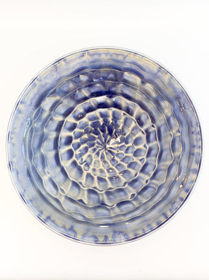 A round ceramic plate with a textured, concentric ripple pattern in blue and white glaze, photographed from directly above on a white background.