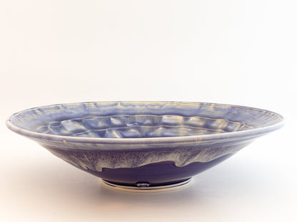 A ceramic bowl with a deep blue and white marbled glaze, featuring a textured pattern inside and a small white foot ring at the base, photographed on a plain white background.