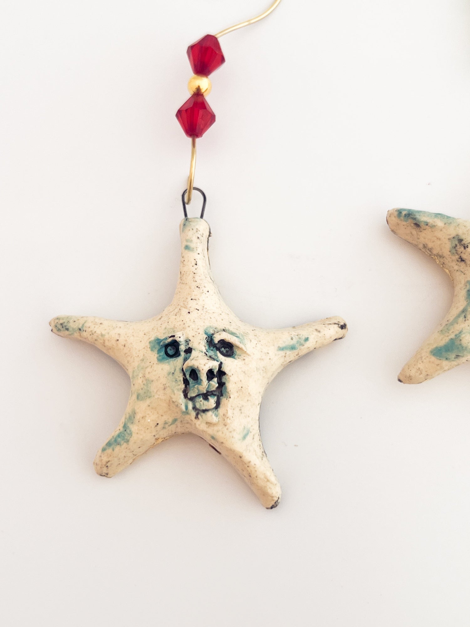 Starfish-shaped ornament with face design and red bead on a white background