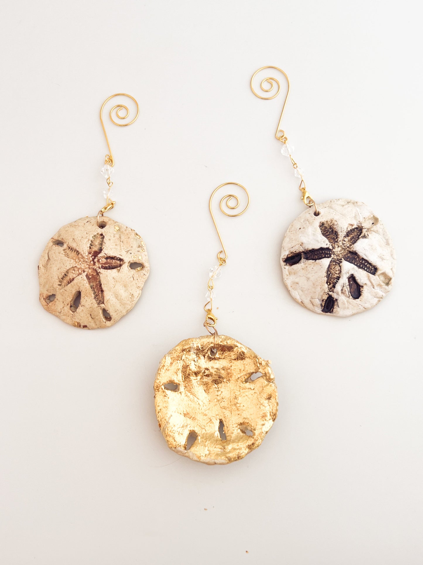 Set of three sand dollar ornaments on a light gray background